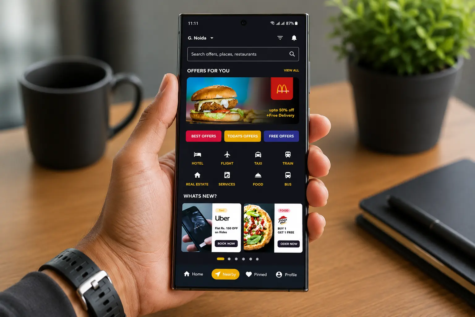 A hand holding a phone that shows Cardinal’s home screen: a search bar, Offers For You with a featured offer, offer categories and a What’s New carousel